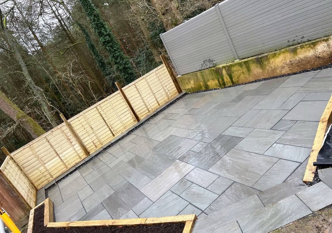 Large patio installation with pale stone paving and timber fencing